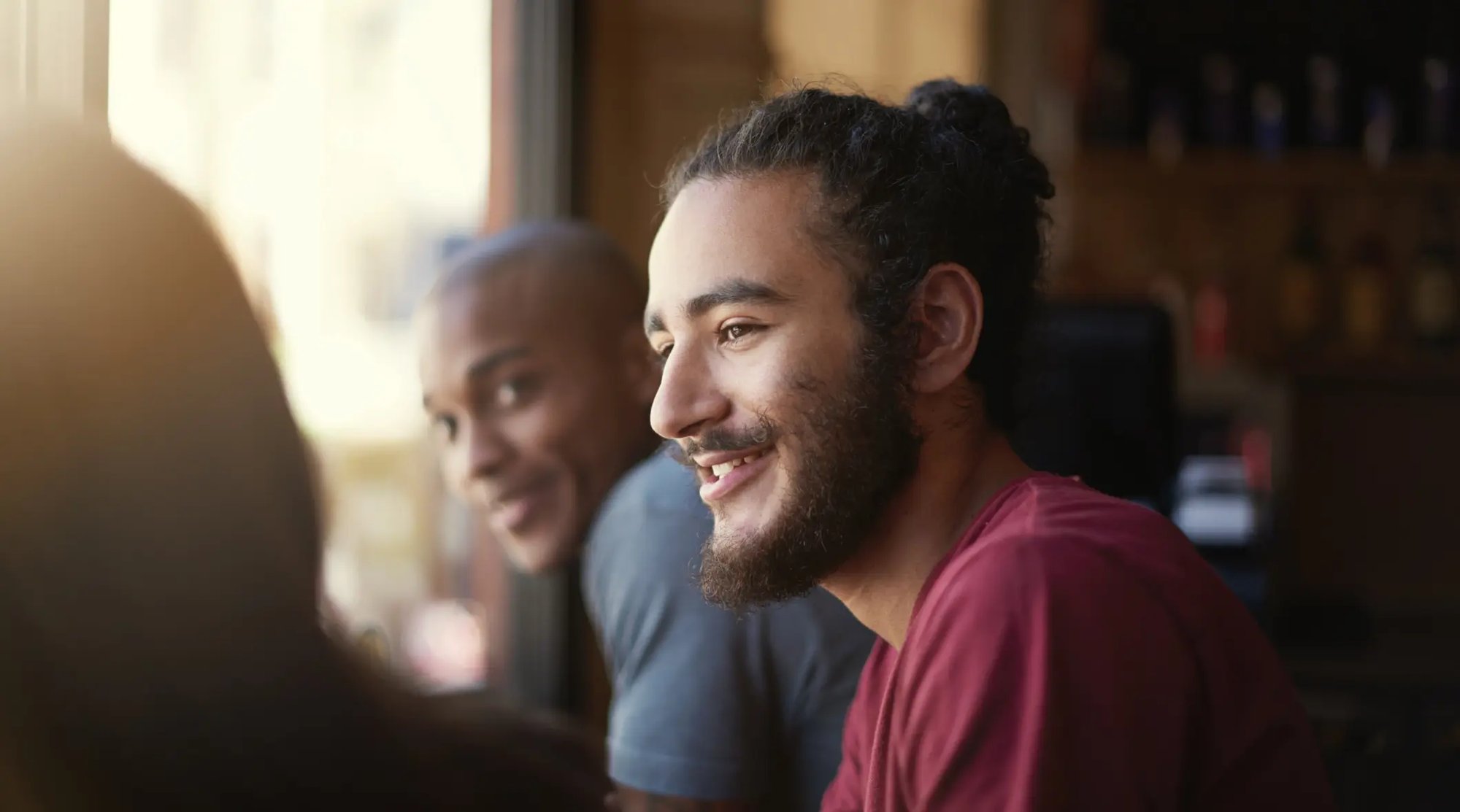 Portrait d'un jeune homme à barbe assis et entouré de personnes devant une fenêtre